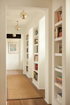 an empty hallway with bookshelves and a rug on the floor in front of it