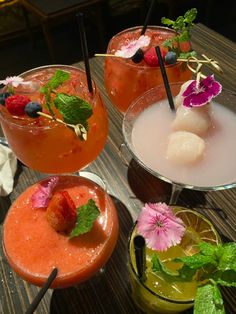 four different types of cocktails on a table with strawberries and blueberries in them