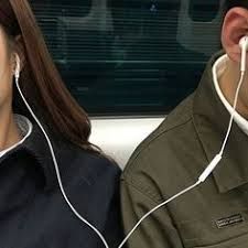 a man and woman sitting next to each other with headphones in their ears, looking out the window