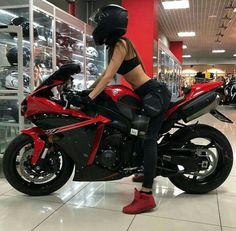 a woman sitting on top of a red motorcycle in a showroom with other motorcycles