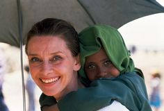 two women with headscarves are smiling under an umbrella