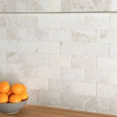 a bowl filled with oranges sitting on top of a wooden table next to a white brick wall