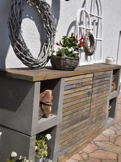 a wooden cabinet with flowers and plants on it's shelf next to a building