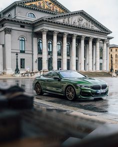 a green car parked in front of a large building on a wet street with people walking by