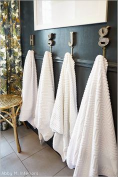 three white towels hanging on hooks in a bathroom