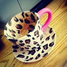 a leopard print coffee cup sitting on top of a wooden table next to a pink handle