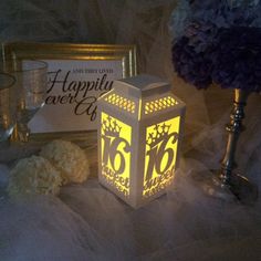 a lit up lantern sitting on top of a bed next to two vases and flowers