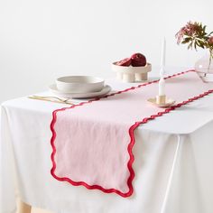 a table topped with a white plate covered in red scalloped trim next to a vase filled with flowers