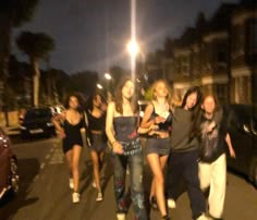 a group of young women walking down the street at night with their laptops open