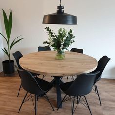 a round wooden table surrounded by black chairs and a potted plant in the center