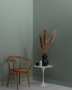 a chair next to a table with a vase on it and a plant in the corner