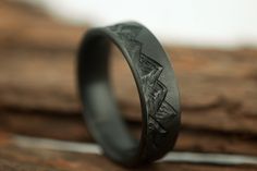 a black ring with an etched design on it sitting on top of a piece of wood