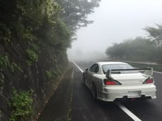 a white sports car driving down a road in the fog