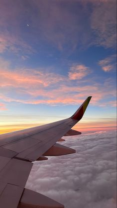 the wing of an airplane as it flies above the clouds at sunset or dawn in the sky