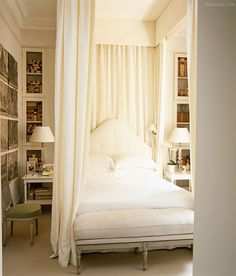 a white bed sitting in a bedroom next to a window with curtains on top of it