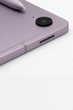 a purple tablet with a pen sitting on it's back cover next to another device