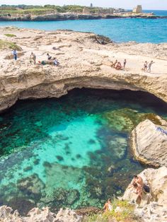 people are swimming in the clear blue water at an ocean cave with rocks and cliffs