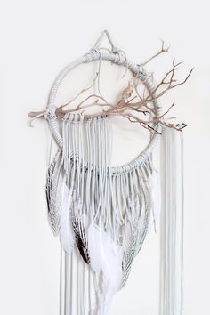 a white dream catcher with feathers and branches hanging from it's sides on a wall