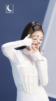 a woman in white dress holding her hand up to her face