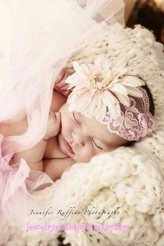 a baby sleeping on top of a white blanket next to a pink and white flower