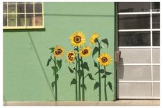 sunflowers painted on the side of a green building in front of a garage door