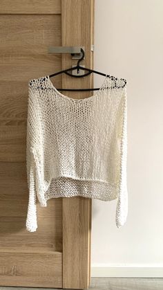 a white sweater hanging from a hook on a wooden door with a hanger in front of it