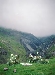 an outdoor ceremony set up with flowers and greenery on the grass in front of mountains