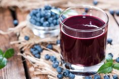 a glass filled with blueberries sitting on top of a wooden table next to some leaves