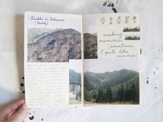 a hand holding an open photo book with mountains in the background and writing on it