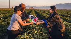 three people in a field with one holding a sign and the other handing something to another person