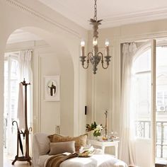 a living room filled with furniture and a chandelier hanging from the ceiling next to two windows