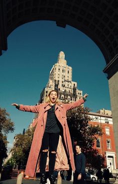 a woman standing in front of a tall building with her arms spread out and hands outstretched