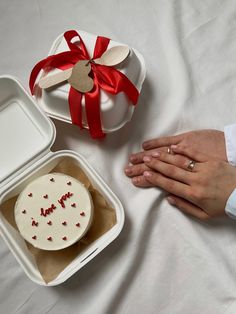 a person holding their hand next to a cake in a box with a red ribbon on it