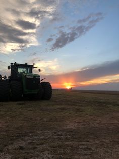 a tractor is parked in an open field at sunset