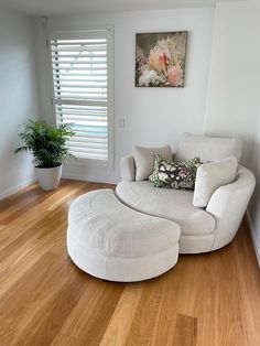 a white chair and ottoman in a room with hardwood floors, windows, and shutters