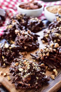 chocolate covered cookies on a wooden cutting board with bowls of nuts and other ingredients in the background