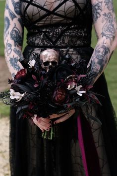 a woman in black dress holding a bouquet with flowers and skulls on her arm,