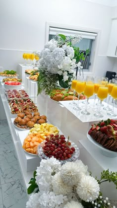 an assortment of fruits and flowers on display in a buffet line with glasses of orange juice