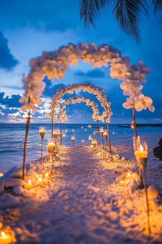 an outdoor wedding set up on the beach at night with candles and flowers in the sand