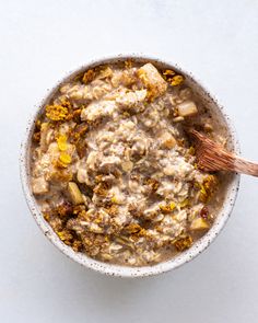 a bowl filled with oatmeal sitting on top of a white table next to a wooden spoon