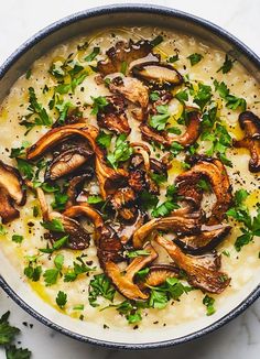 a bowl of soup with mushrooms, parsley and lemon wedges on the side