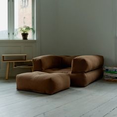 a brown chair and ottoman in a room with white flooring next to a window