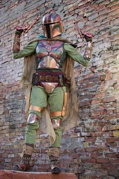 a man dressed as boba fett standing in front of a brick wall with his arms outstretched