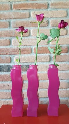 three pink vases with flowers in them sitting on a red table next to a brick wall