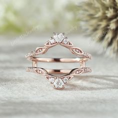 two rose gold wedding rings with diamonds on the top and bottom, sitting next to a pine tree