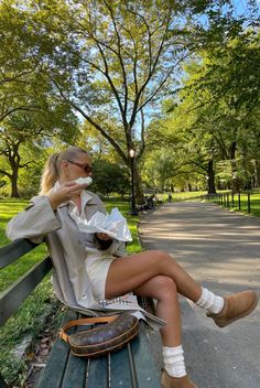 a woman sitting on top of a wooden bench next to a park filled with trees