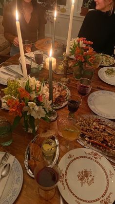 a group of people sitting around a table with food and candles in the middle of it