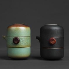 two ceramic teapots sitting next to each other on a gray surface, one is green and the other is black