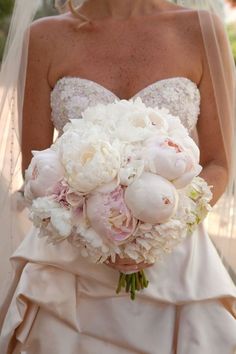 a woman in a wedding dress holding a bridal bouquet with white and pink flowers