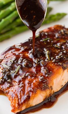 a piece of salmon covered in bbq sauce being drizzled over asparagus